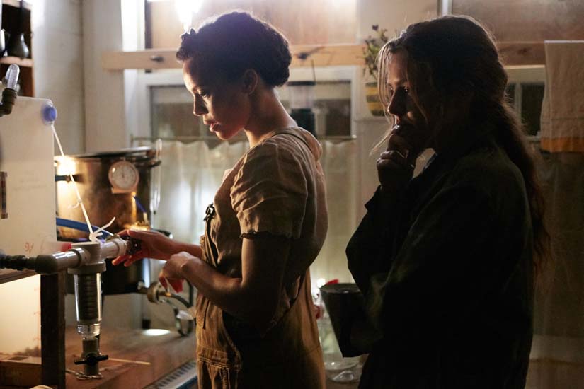 Two women stand tensely next to a water filtration system