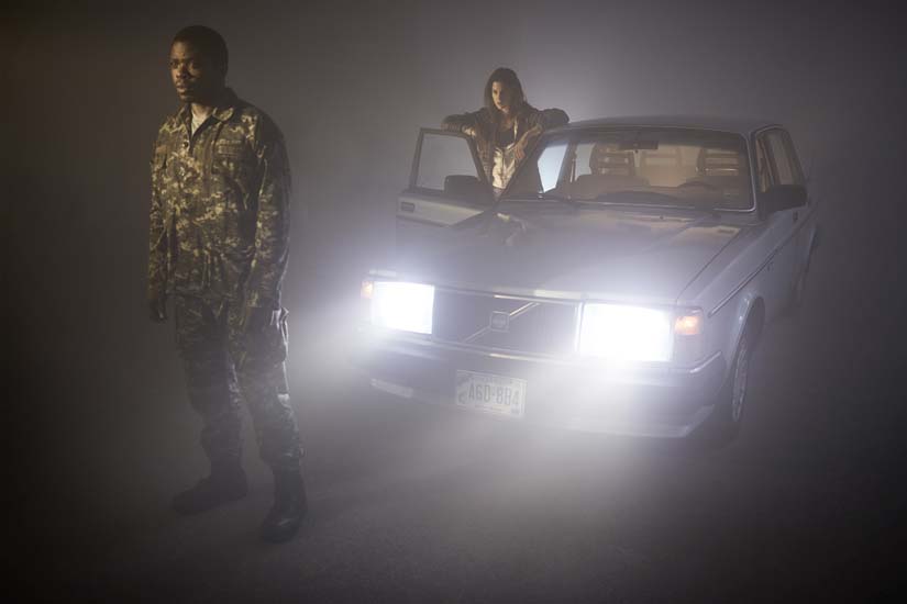 Two people stand outside a car at night peering ahead