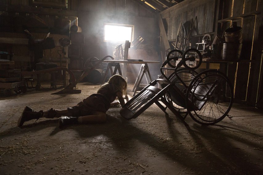 A girl crawls on a barn floor next to an overturned wheelchair