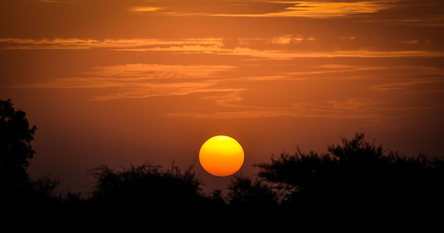 The sun sets in a dark orange sky.