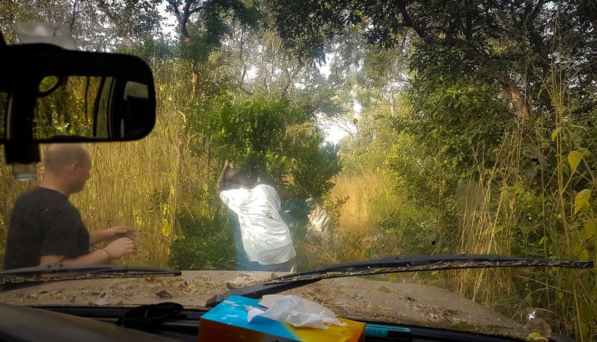 From the passenger seat, one can see two men trying to clear a path through the brush.