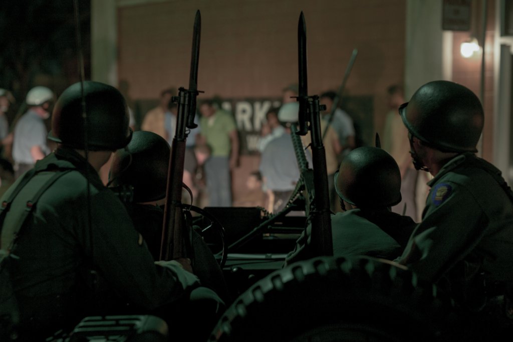 Heavily-armed National Guardsmen look upon a police force approaching a group backed by a brick wall.