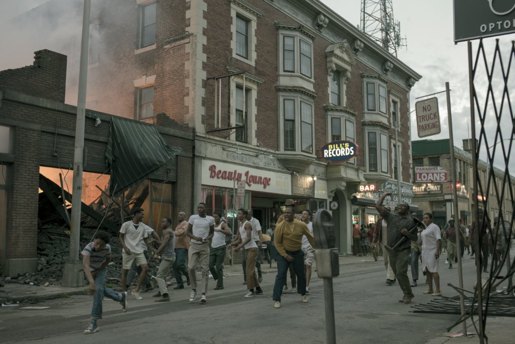 People walk through a destroyed part of town yelling and throwing rocks.