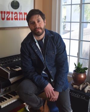 A man with brown hair and a beard leans against a keyboard.