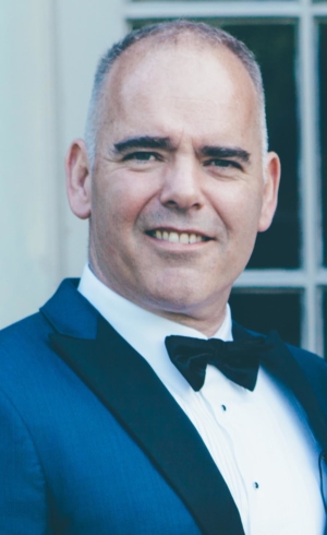 A older gentleman smiles wearing a suit and bow tie.