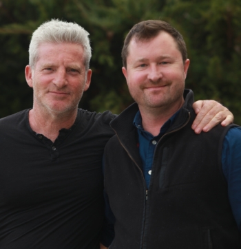 A man with grey hair and a man with brown hair smile for the camera.