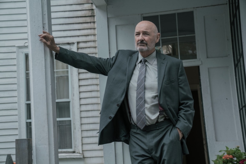 Dale Lacy (Terry O'Quinn) leans on the beam of his front porch.