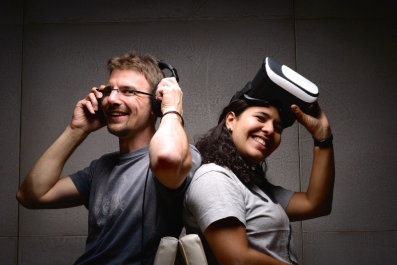 A man wears headphones and a woman wears a VR device