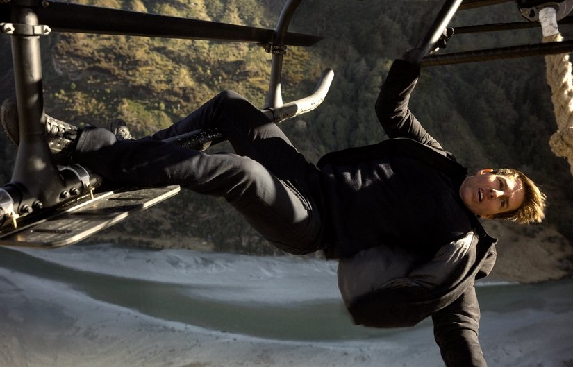 Tom Cruise hangs from the helicopter landing skid.