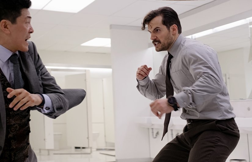Henry Cavill bows up and looks fiercely at a man in a business suit.
