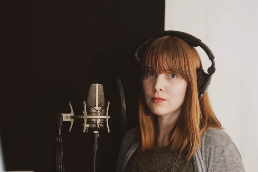 Mary Kate Jiménez - a woman with long red hair stands next to a vocal mic.
