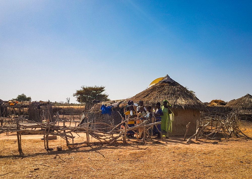 A group of women and children stand outside a hut.