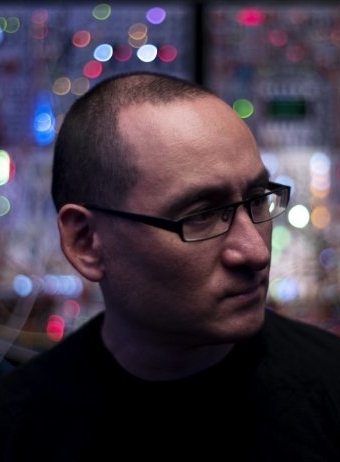 A man with close cut hair and glasses looks away