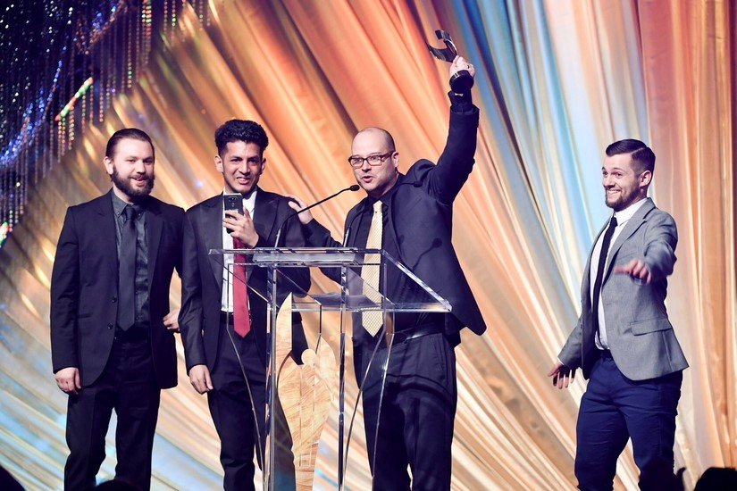 4 men stand on a brightly lit stage celebrating their award.