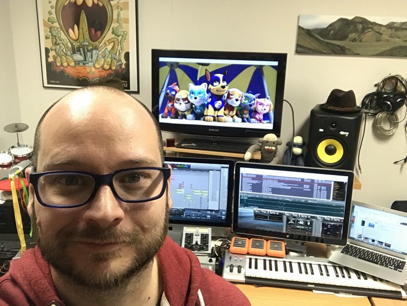 A man in glasses sits in front of his workspace with Mighty Pups on the computer screen.
