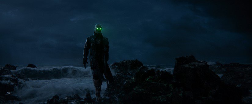 A dark machine with bright green eyes walks through a desolate field at night.