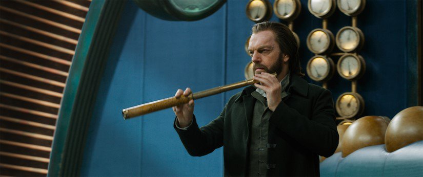 Hugo Weaving holds a handheld telescope to his face.