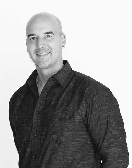 A man with a short beard and button-up shirt smiles.