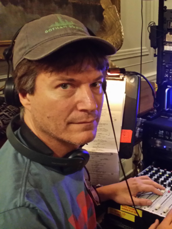 A man wearing a baseball cap sits at his soundboard.