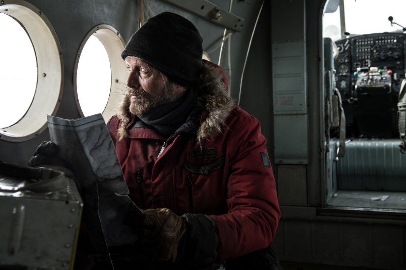 A man in a plane wearing winter gear holds a map.