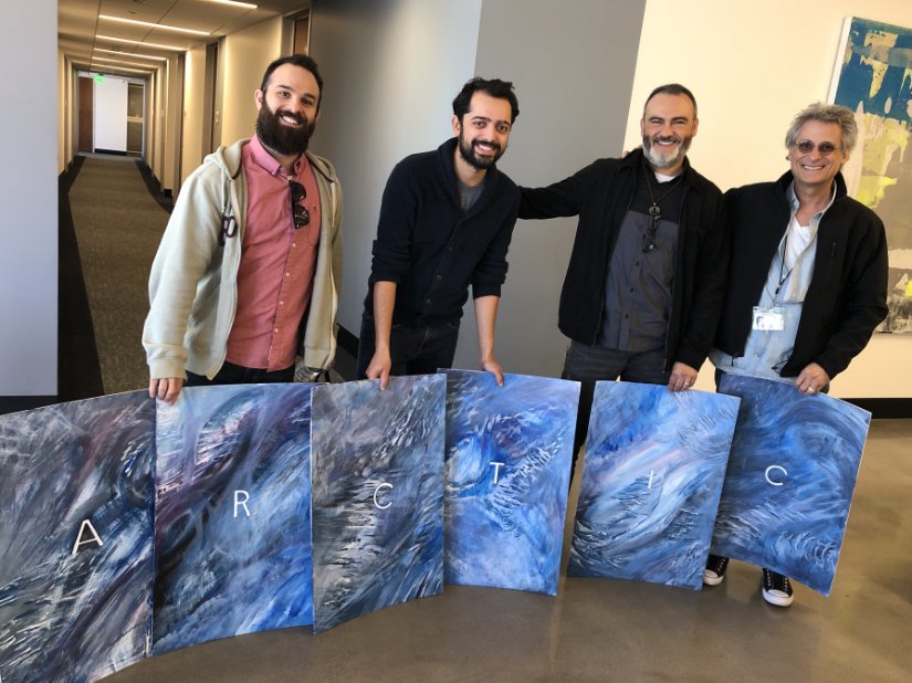 4 men stand behind painted boards that create the word "Arctic"