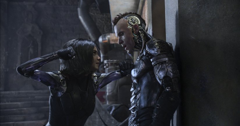 Alita, a robotic woman, pins Zapan, a robotic man, against a wall.