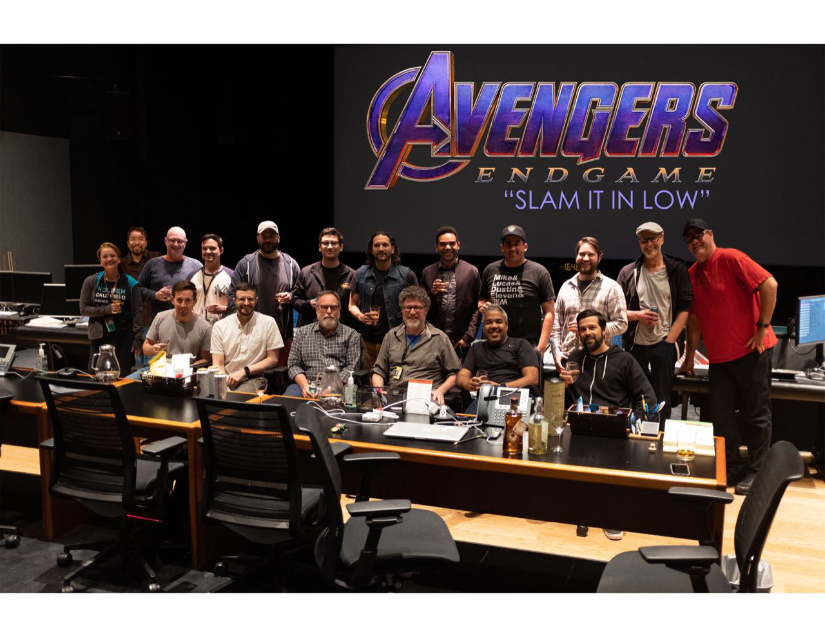18 sound designers sit and stand in front of the theater screen showing the Avengers: Endgame title