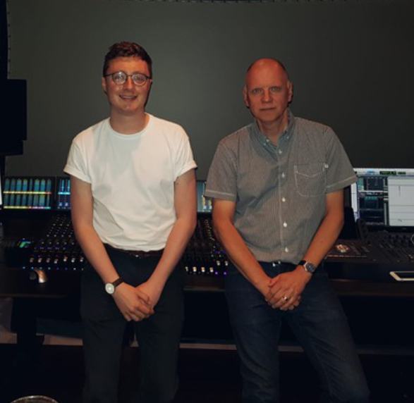 Two men stand at their workstation